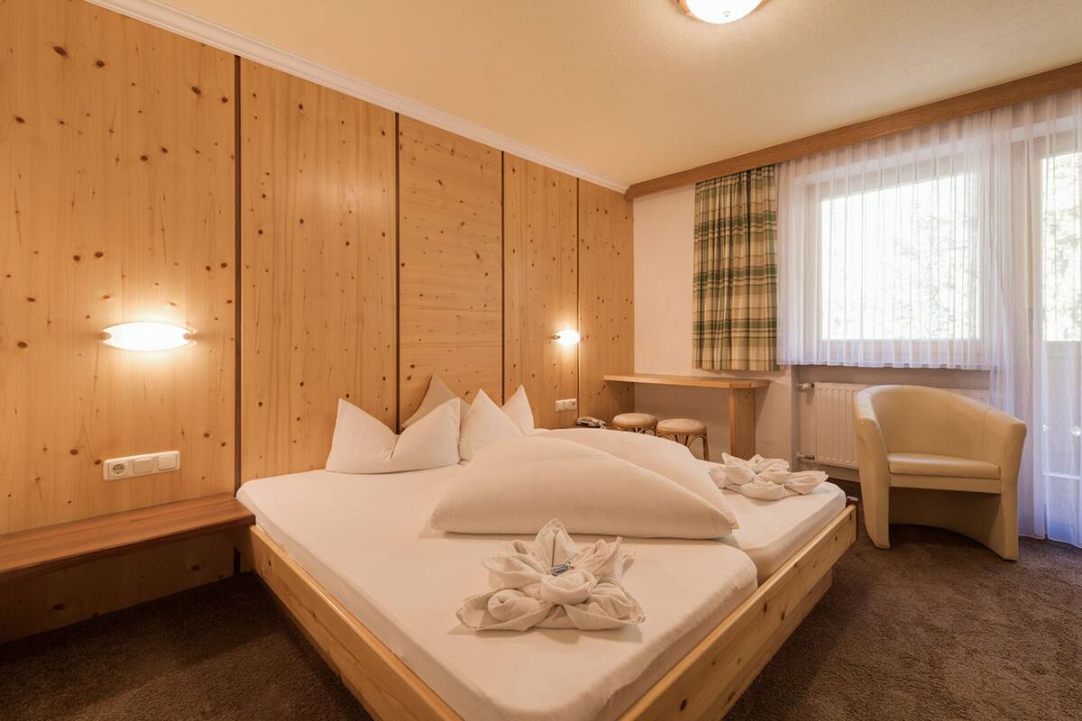 A hotel room with a wooden panel wall, a bed with white linens, a chair, and a small table.