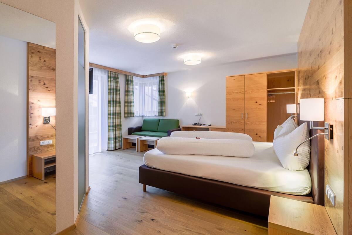 A modern hotel room with a wooden floor, a bed, a green sofa, a desk, and a wardrobe.