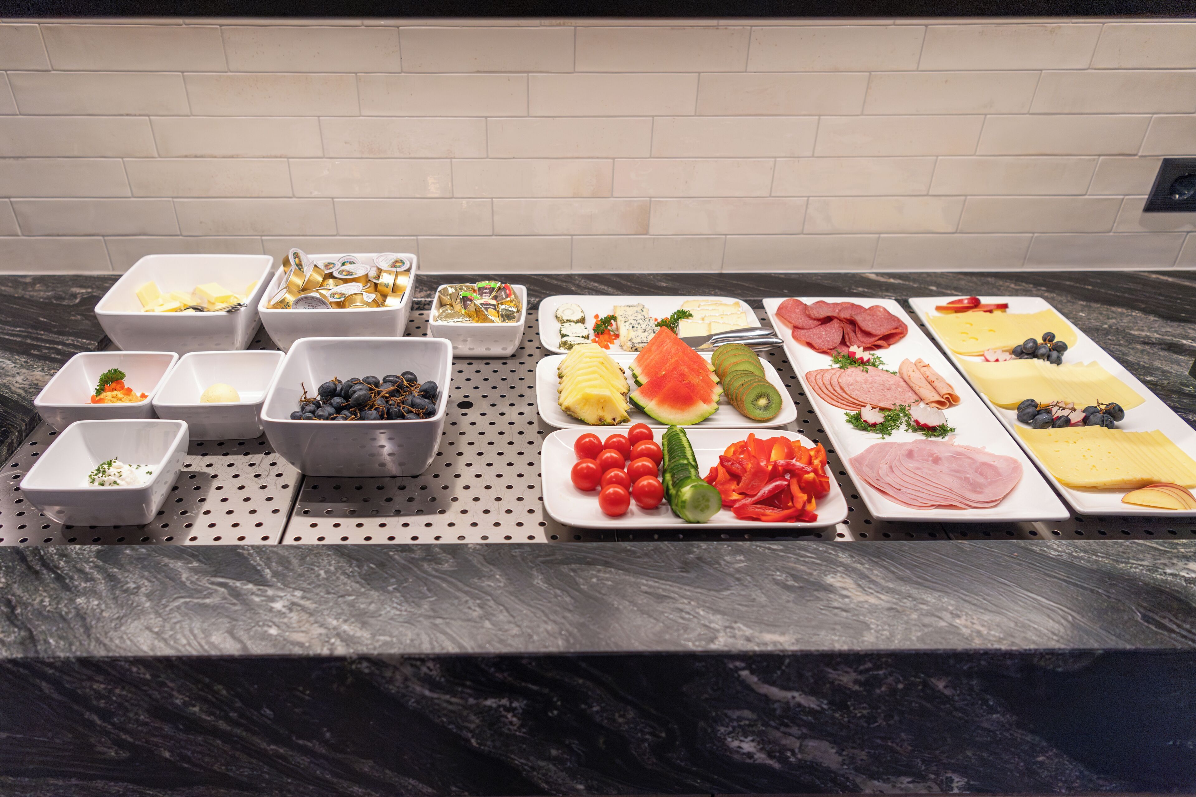 A buffet table with various food items including fruits, vegetables, cheeses, and meats.