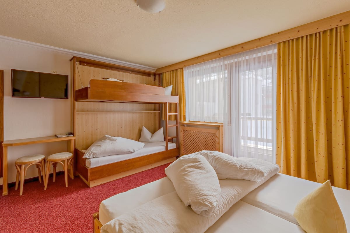 A room with a bunk bed, a desk with a chair, and a bed with pillows.