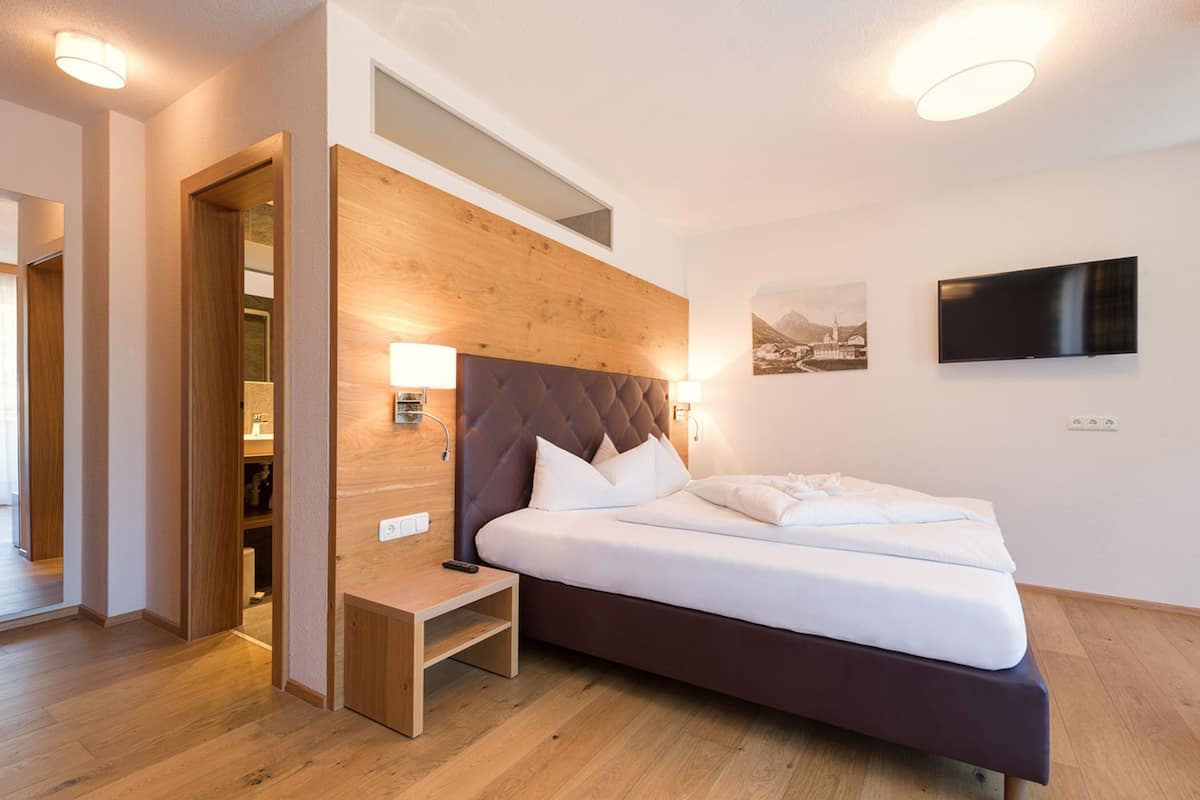 A modern hotel room with a wooden headboard, a flat-screen TV, and a bed with white linens.
