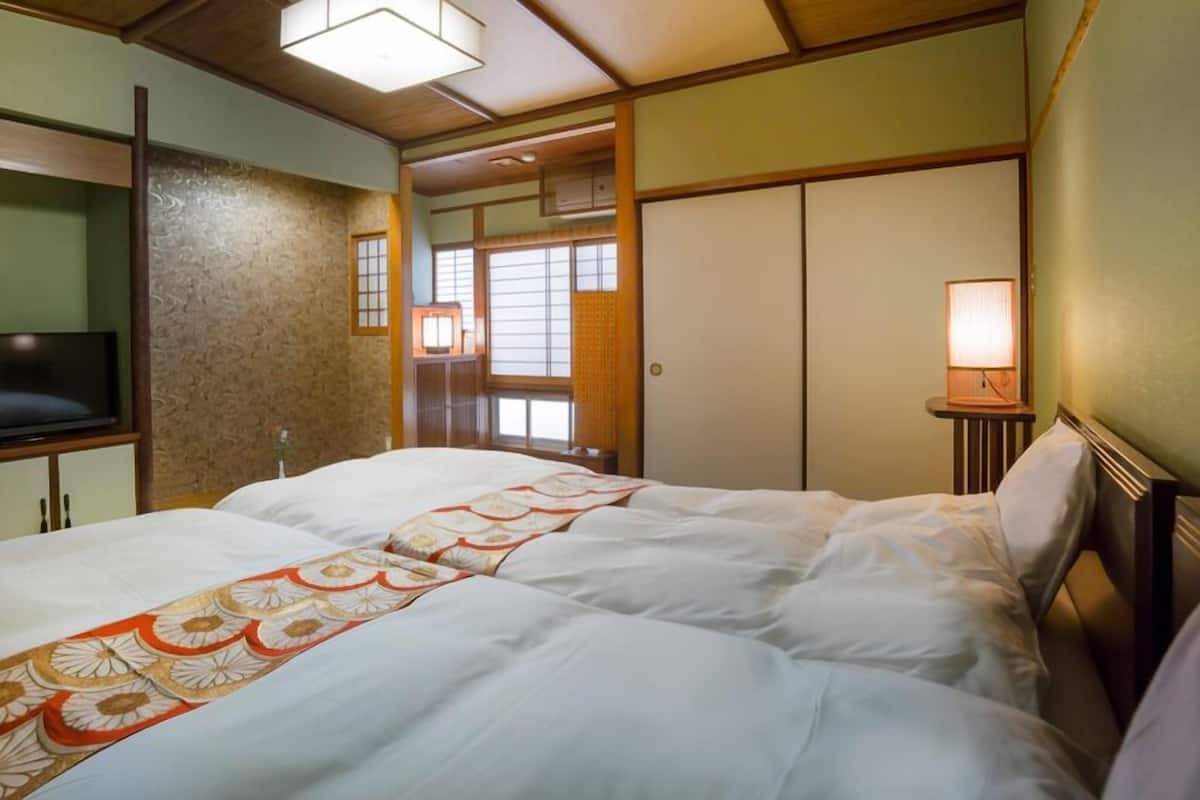 Een hotelkamer met een bed, een televisie, een bedlamp en een raam met jaloezieën.