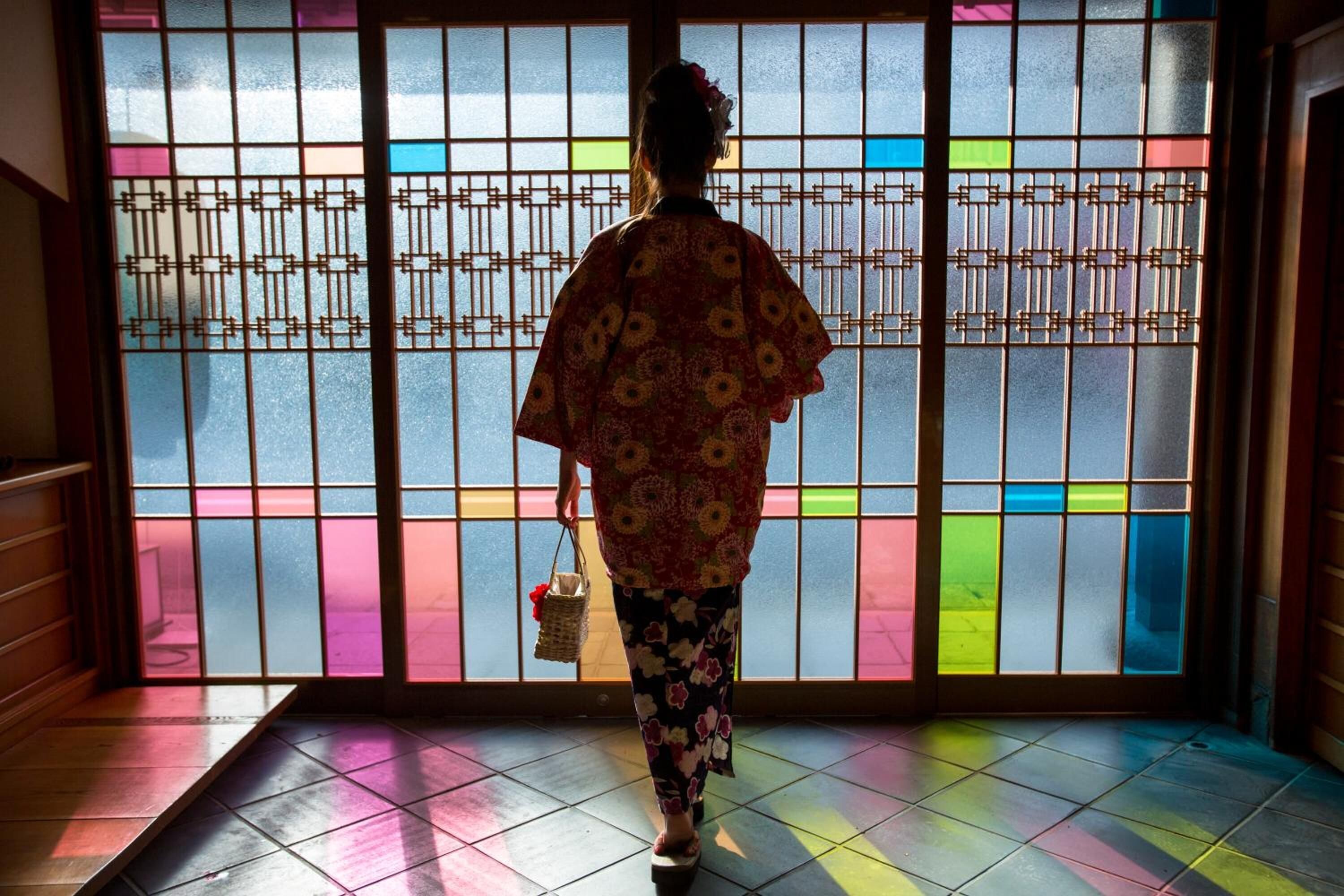 A person in traditional attire walking towards a shoji screen with a geometric pattern.