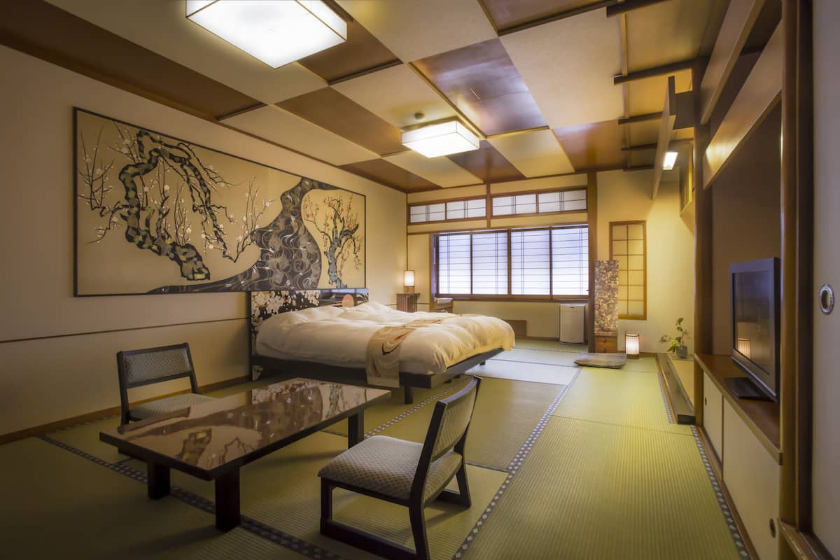 Een traditionele Japanse kamer met tatami vloeren, een bed, een televisie en een groot kunstwerk aan de muur.