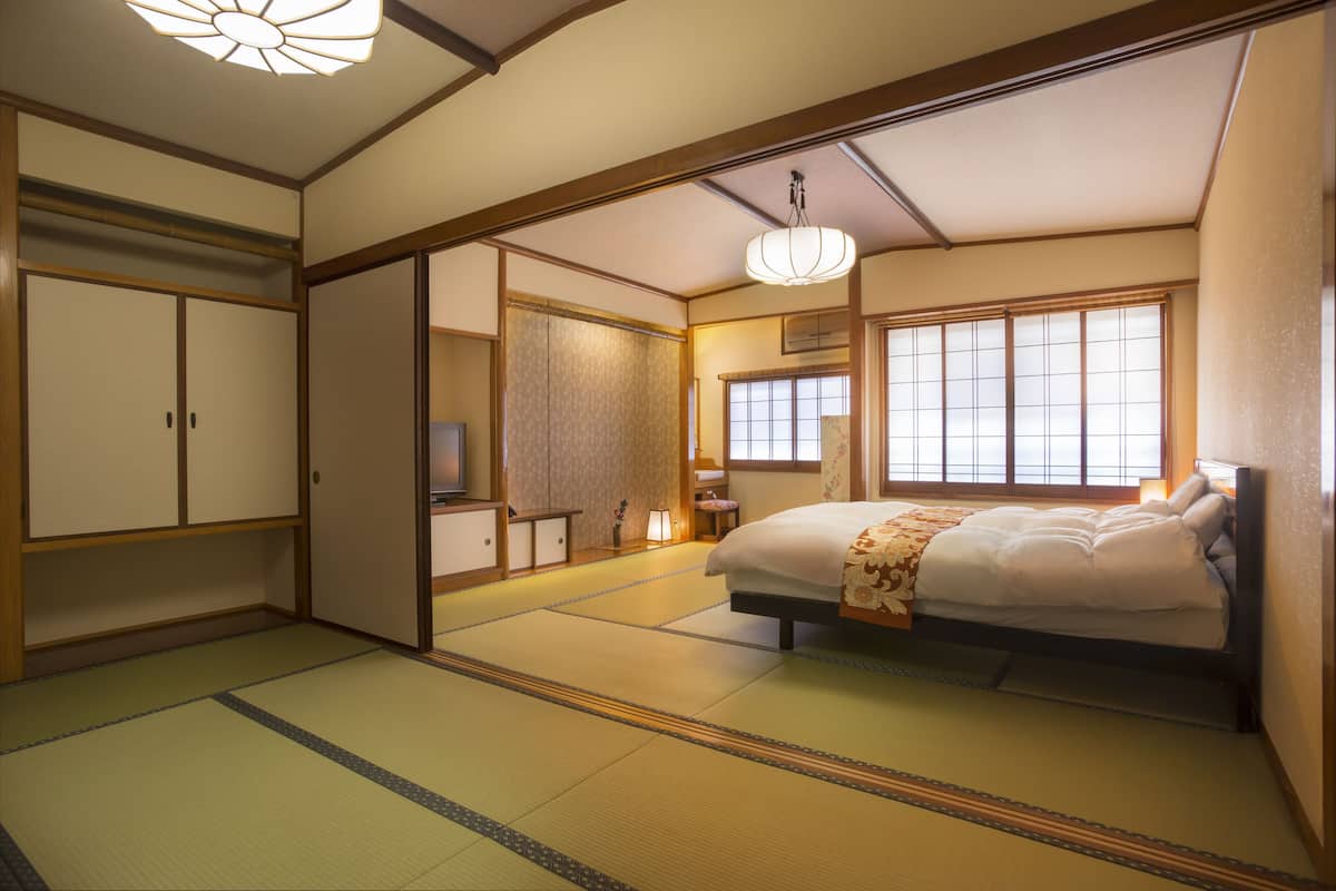 Een traditionele Japanse slaapkamer met tatami vloerbedekking, een bed met bloemenprint, een televisie en schuifdeuren.