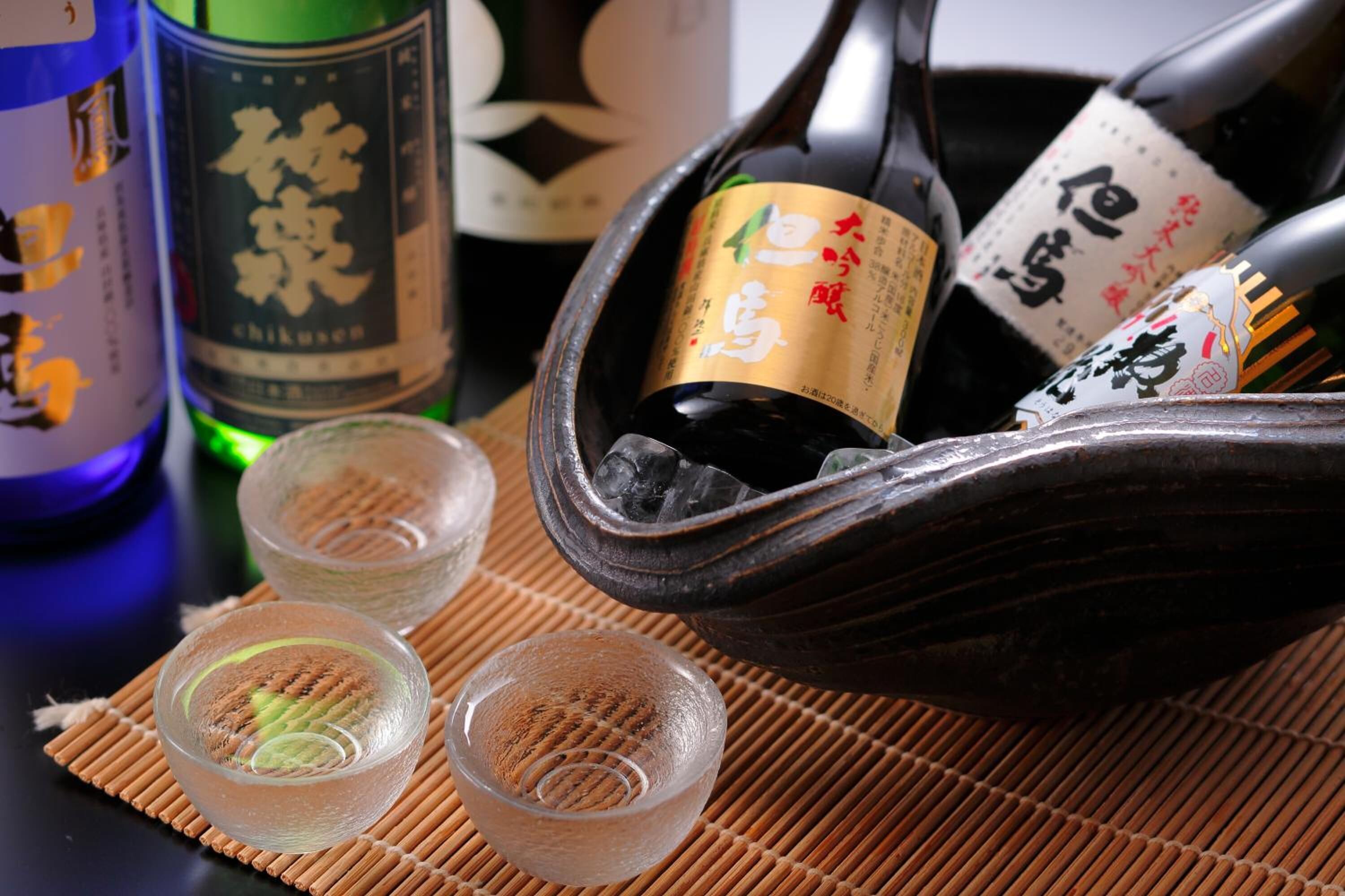 Un juego tradicional japonés de sake con botellas y copas pequeñas sobre una estera de bambú.