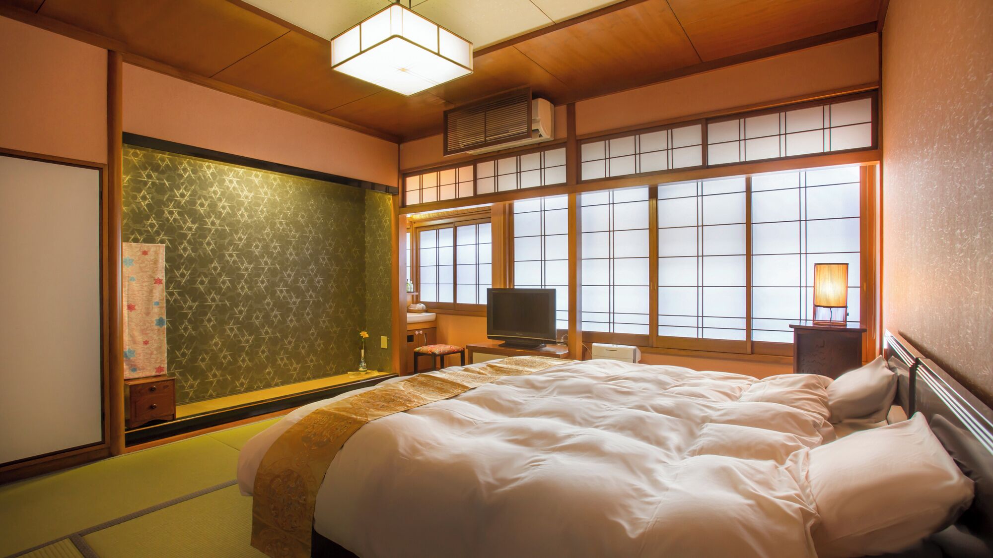 A traditional Japanese-style room with tatami flooring, a bed with white bedding, a television, and a window with shoji screens.
