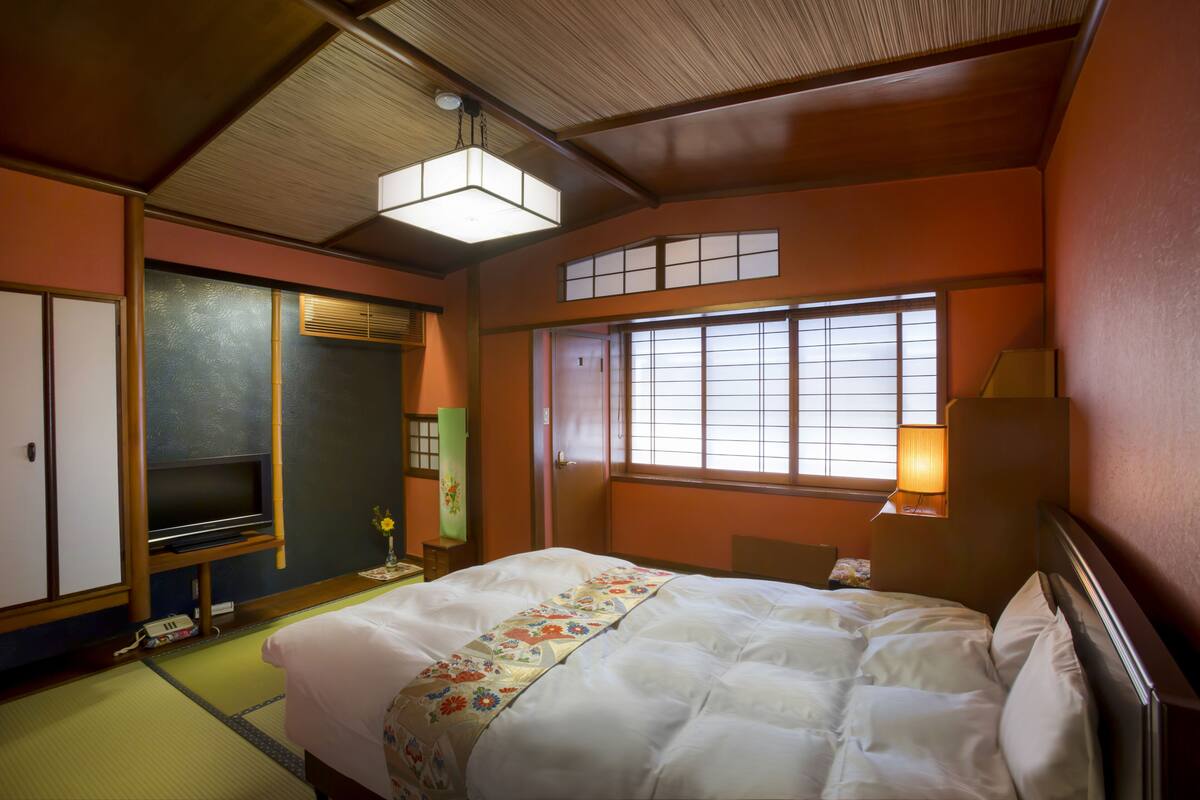 Een traditionele Japanse hotelkamer met tatami vloeren, een futon bed, schuifdeuren en een televisie.