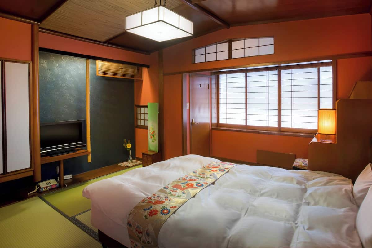 A traditional Japanese-style hotel room with tatami flooring, a bed with a floral bedspread, a television, and sliding doors.
