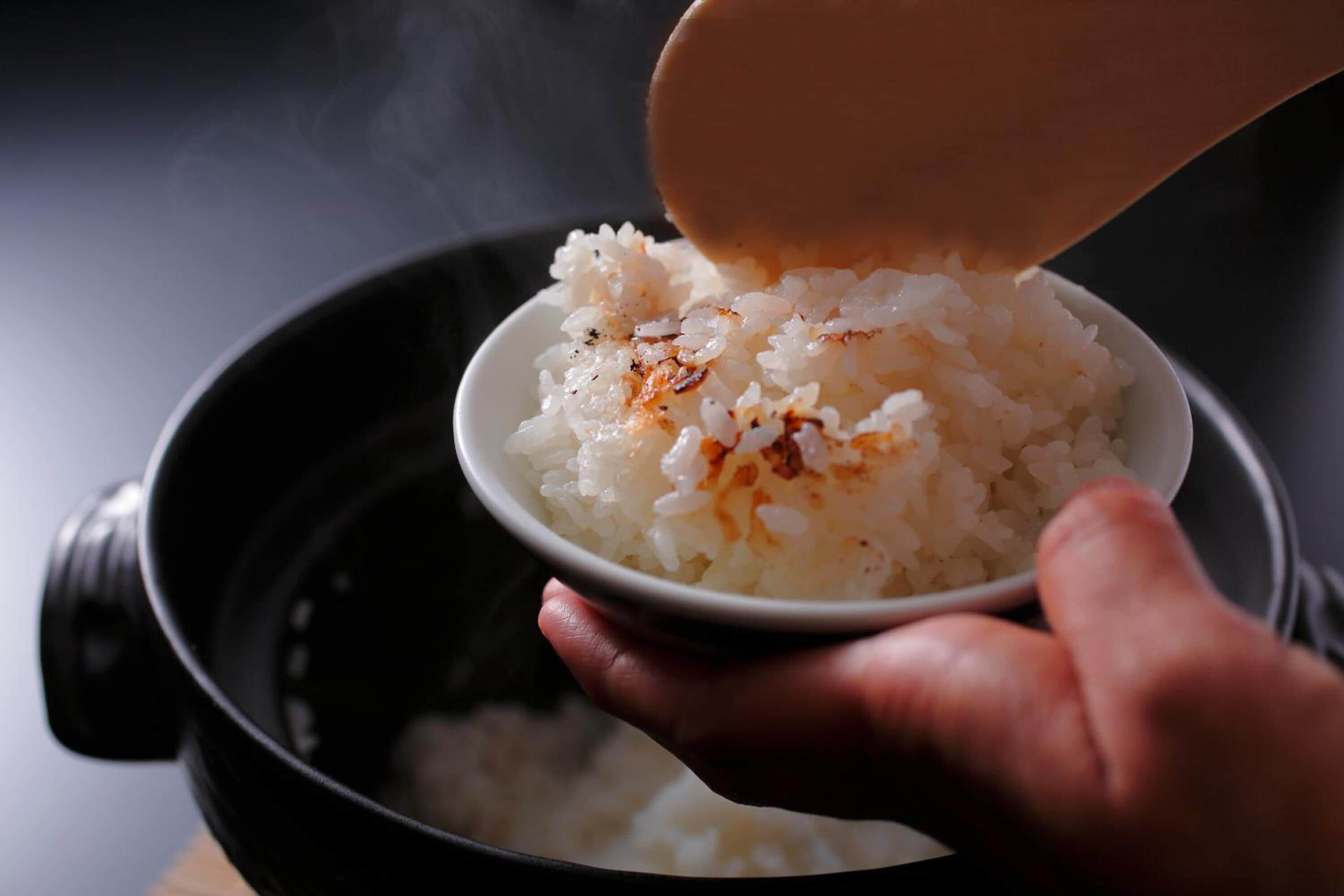 A hand holding a bowl of cooked rice with a spoon pouring more rice into it.