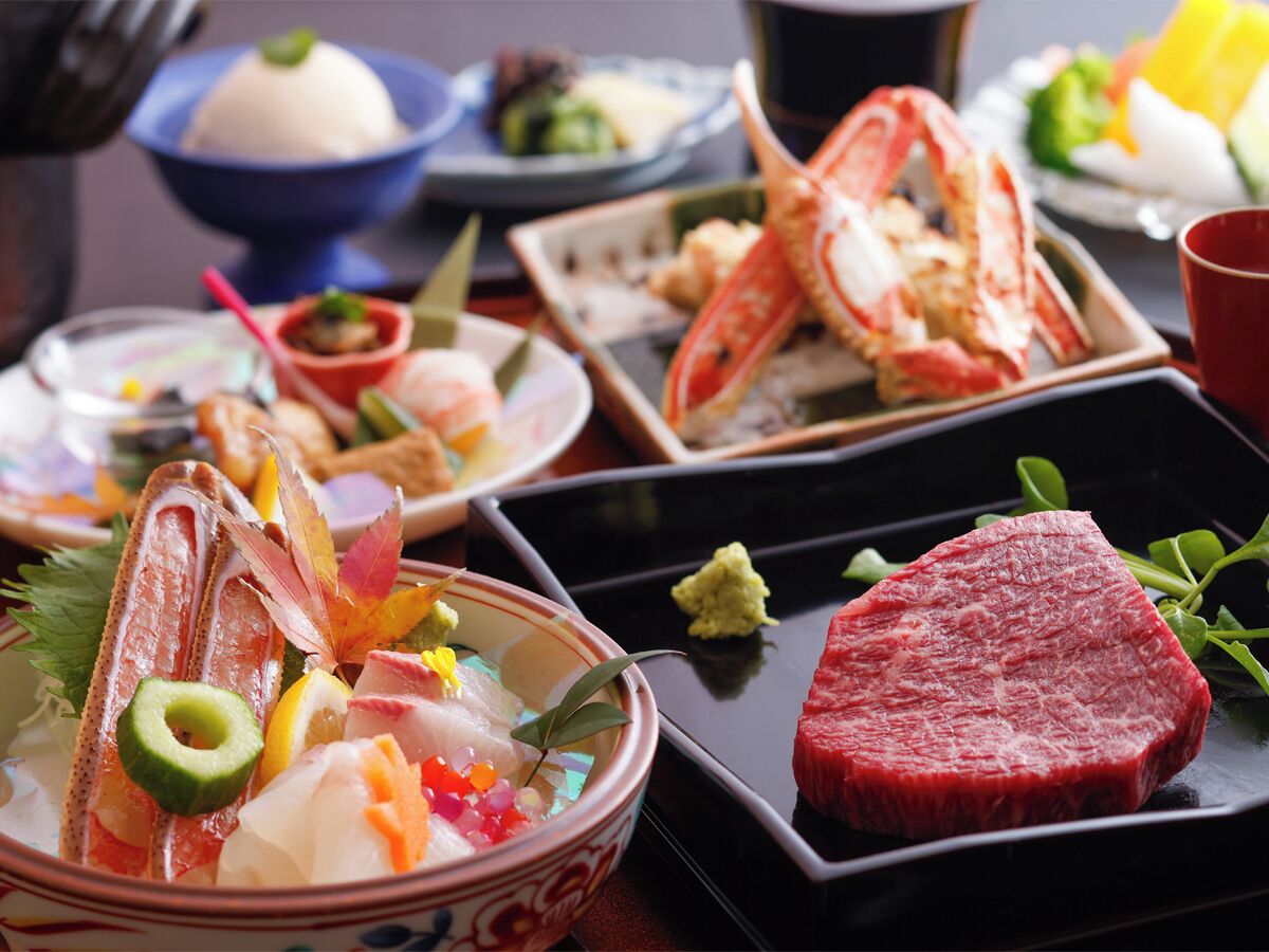 A variety of dishes including seafood, a steak, and a bowl of soup, arranged on a table.