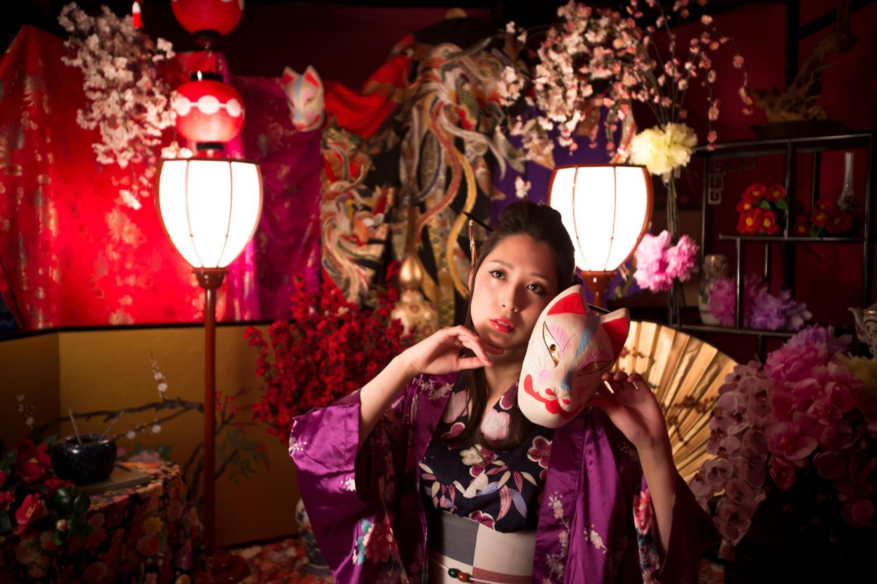 A person in a room with traditional decor, including a fan, flowers, and a lantern.