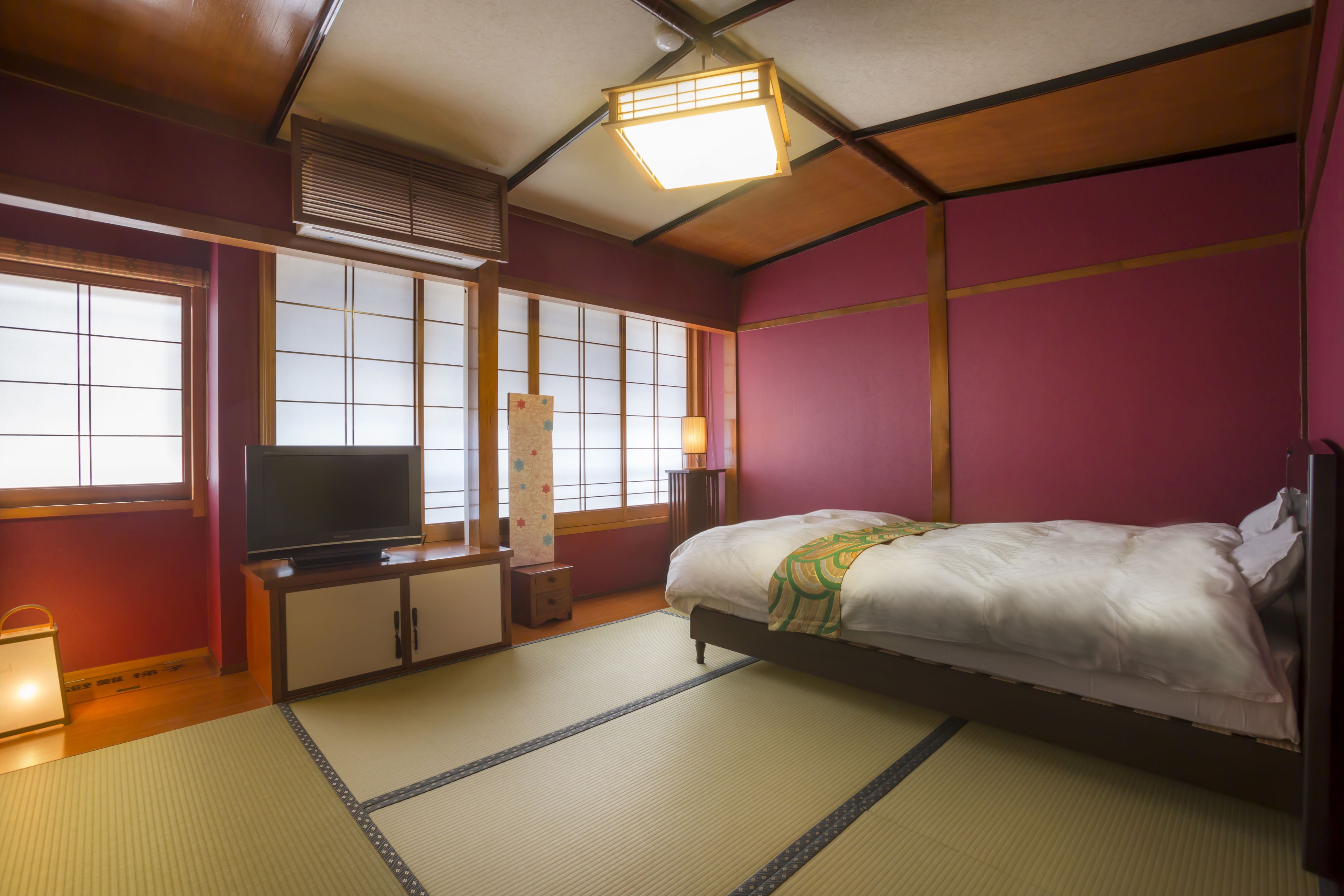 A traditional Japanese-style bedroom with tatami flooring, a bed, a television, and sliding doors.