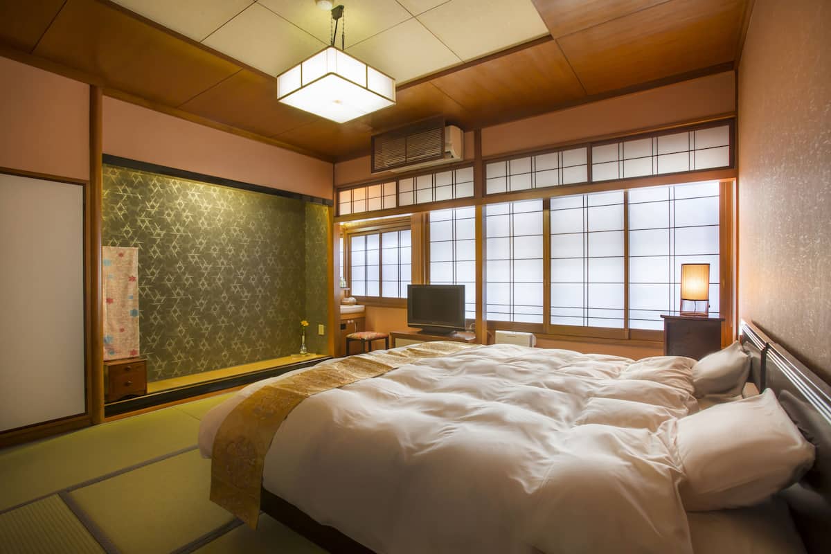 Een traditionele Japanse slaapkamer met tatami vloerbedekking, een groot bed met witte beddengoed, een televisie en een schuifdeur van shoji-papier.