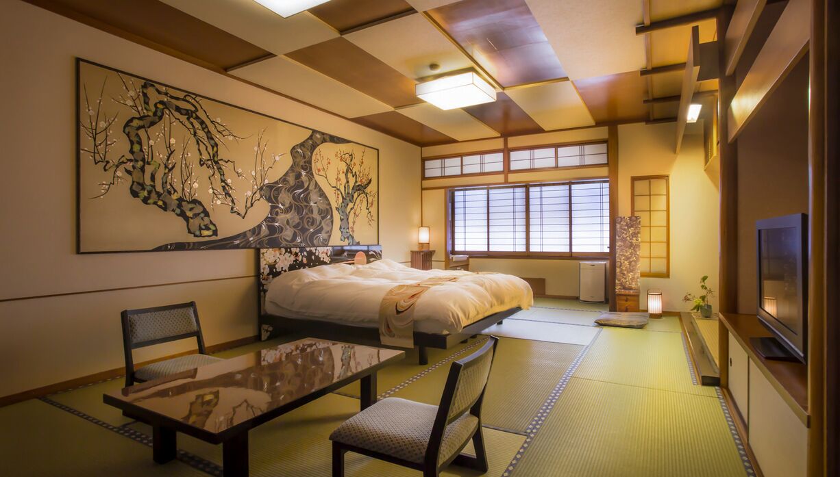 Una habitación japonesa tradicional con suelo de tatami, una cama, un televisor y obras de arte en las paredes.