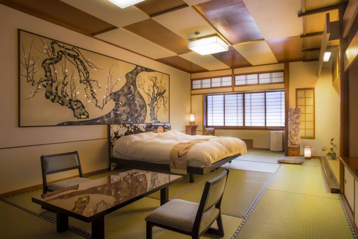 Een traditionele Japanse kamer met tatami vloerbedekking, een bed, een televisie en kunstwerken aan de wanden.