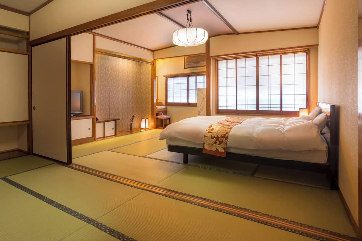 A traditional Japanese room with tatami flooring, a bed with a decorative bedspread, sliding doors, and a television.