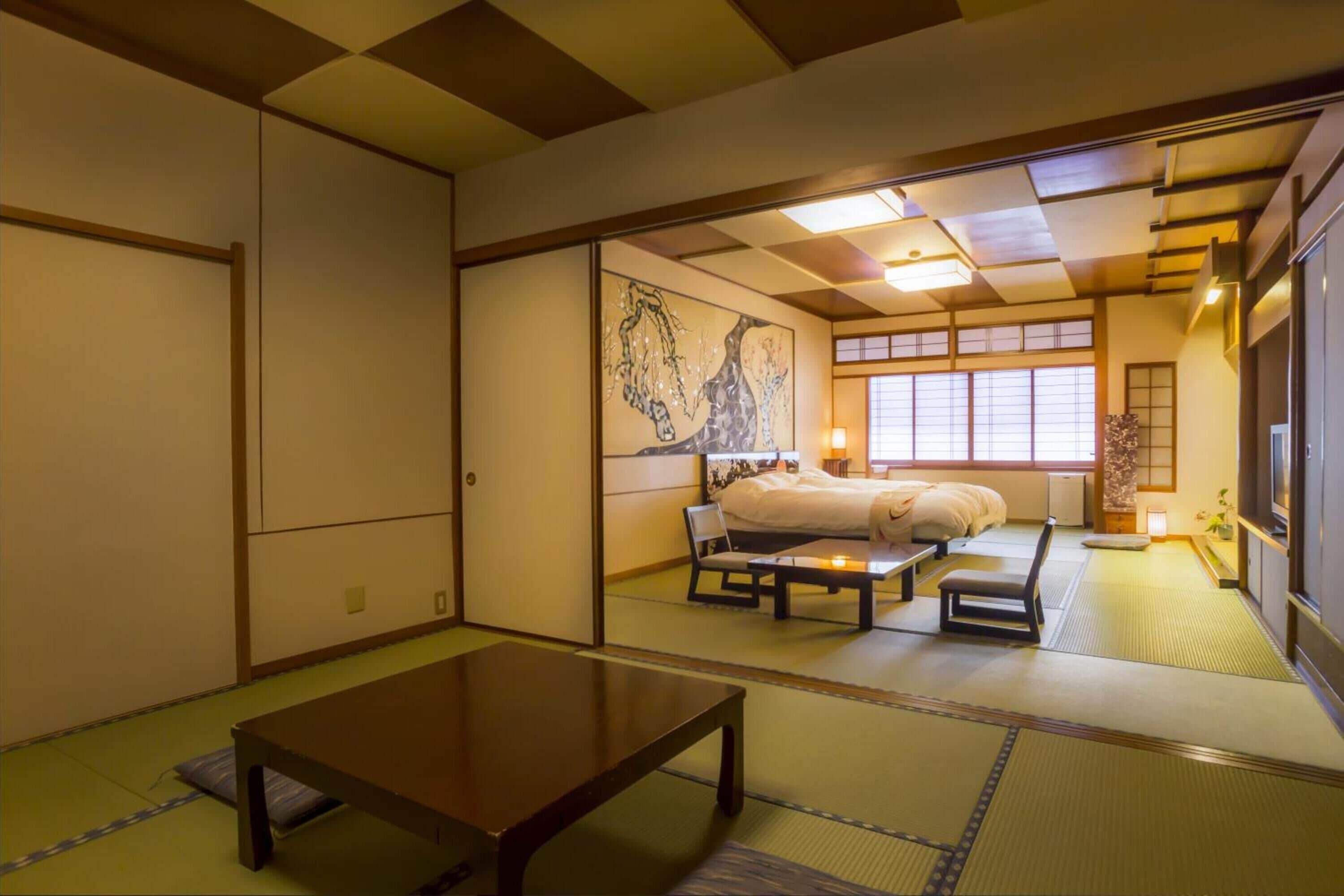 Une pièce de style japonais traditionnel, avec un sol recouvert de tatamis, une table basse, un lit avec une couette blanche et un grand tableau accroché au mur.