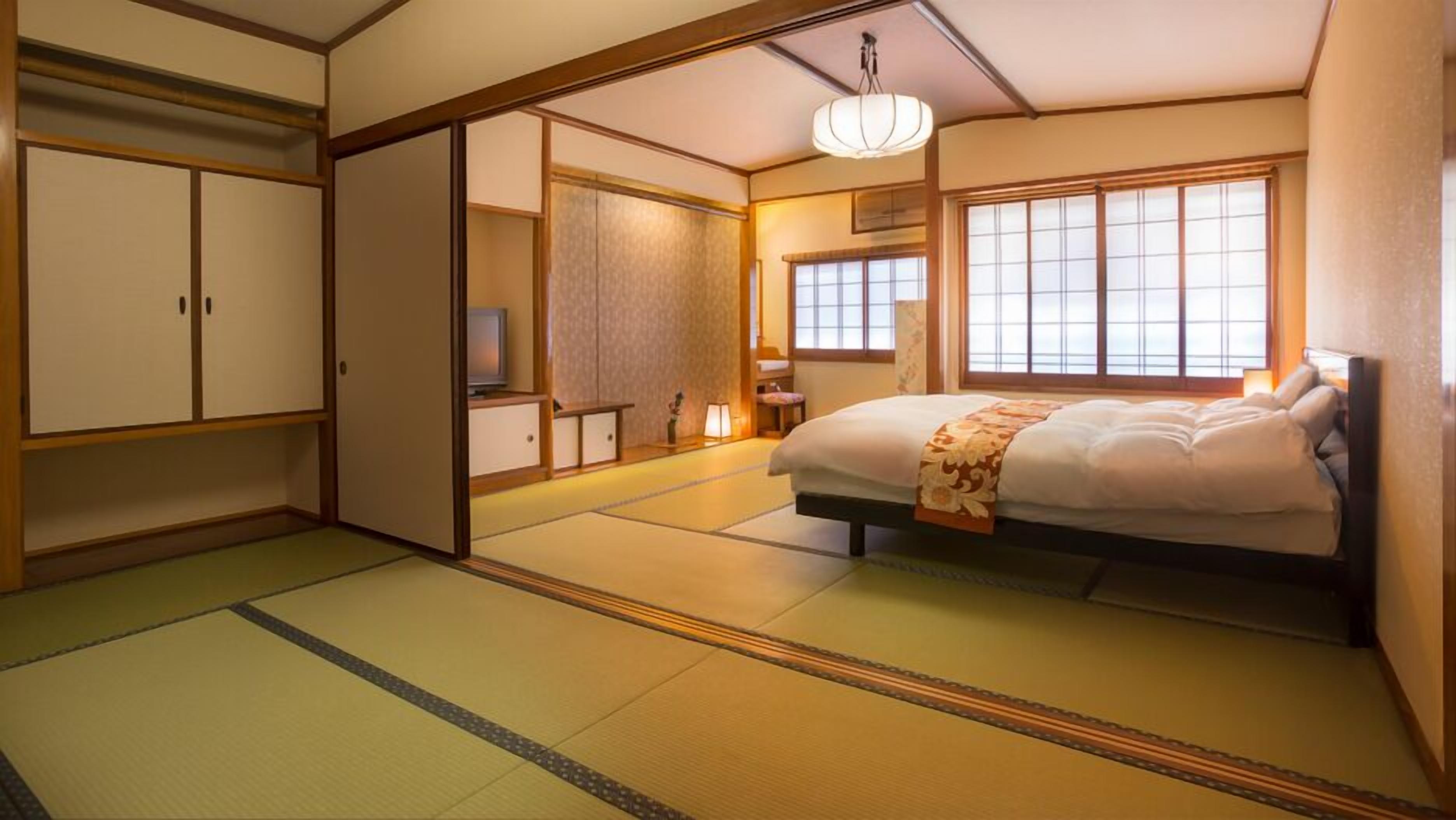 Una habitación de estilo japonés tradicional con suelo de tatami, una cama con edredón floral, puertas correderas y un televisor.