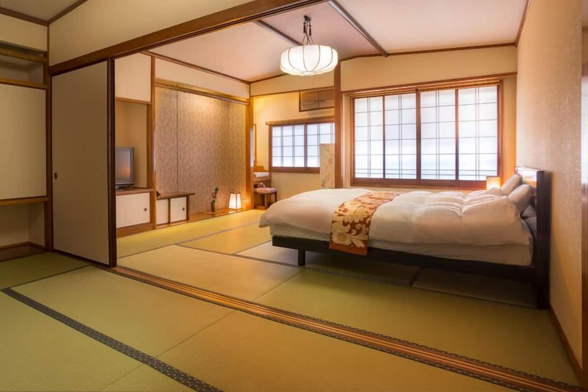 Een traditionele Japanse kamer met tatami vloerbedekking, een bed met een bloemenprint sprei, schuifdeuren en een televisietoestel.