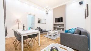 A modern living room with a white dining table, grey sofa, and a chandelier. - Dominik Apartment (Budapest)