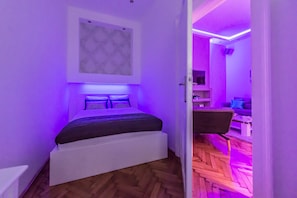 A modern bedroom with a bed, a wall-mounted artwork, and a herringbone-patterned wooden floor. - Dominik Apartment (Budapest)