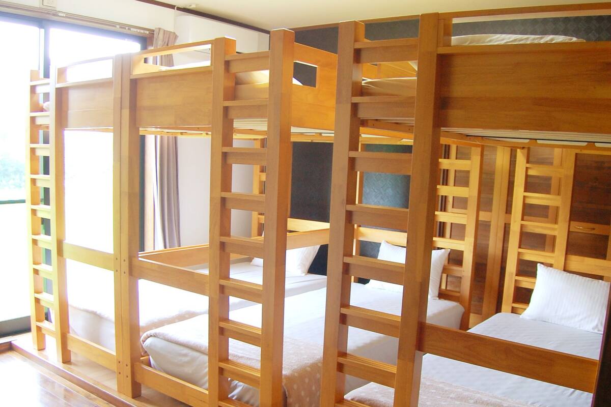 A room with bunk beds, wooden railings, and a window with curtains.