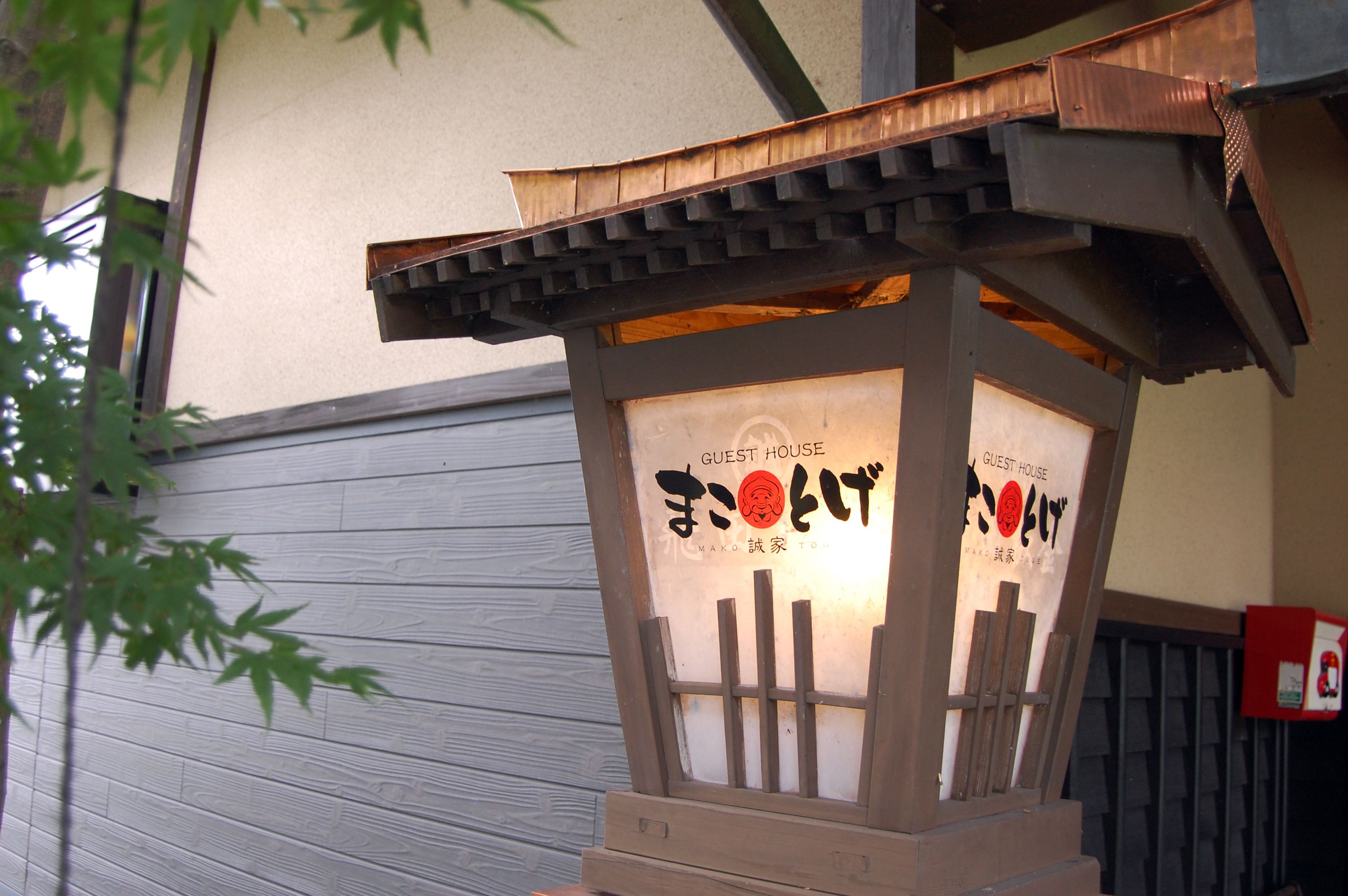 A wooden guest house with a traditional Japanese design, featuring a sloped roof and a sign with Japanese characters.