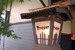 A wooden guest house with a traditional Japanese design, featuring a sloped roof and a sign with Japanese characters. - Guest House MAKOTOGE - Hostel (Aso)