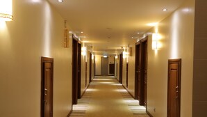 A hotel hallway with wooden doors, carpeted floors, and wall-mounted lighting. - Pacific Hotel (Yangon)