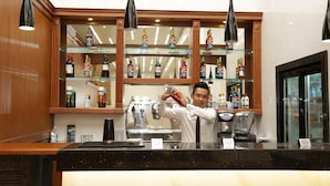 A bar area with shelves of liquor bottles, a coffee machine, and a person pouring a drink. - Pacific Hotel (Yangon)