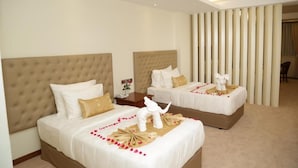 A hotel room with two beds, each with a tufted headboard, white bedding, and decorative elements like a white elephant statue and rose petals. - Pacific Hotel (Yangon)