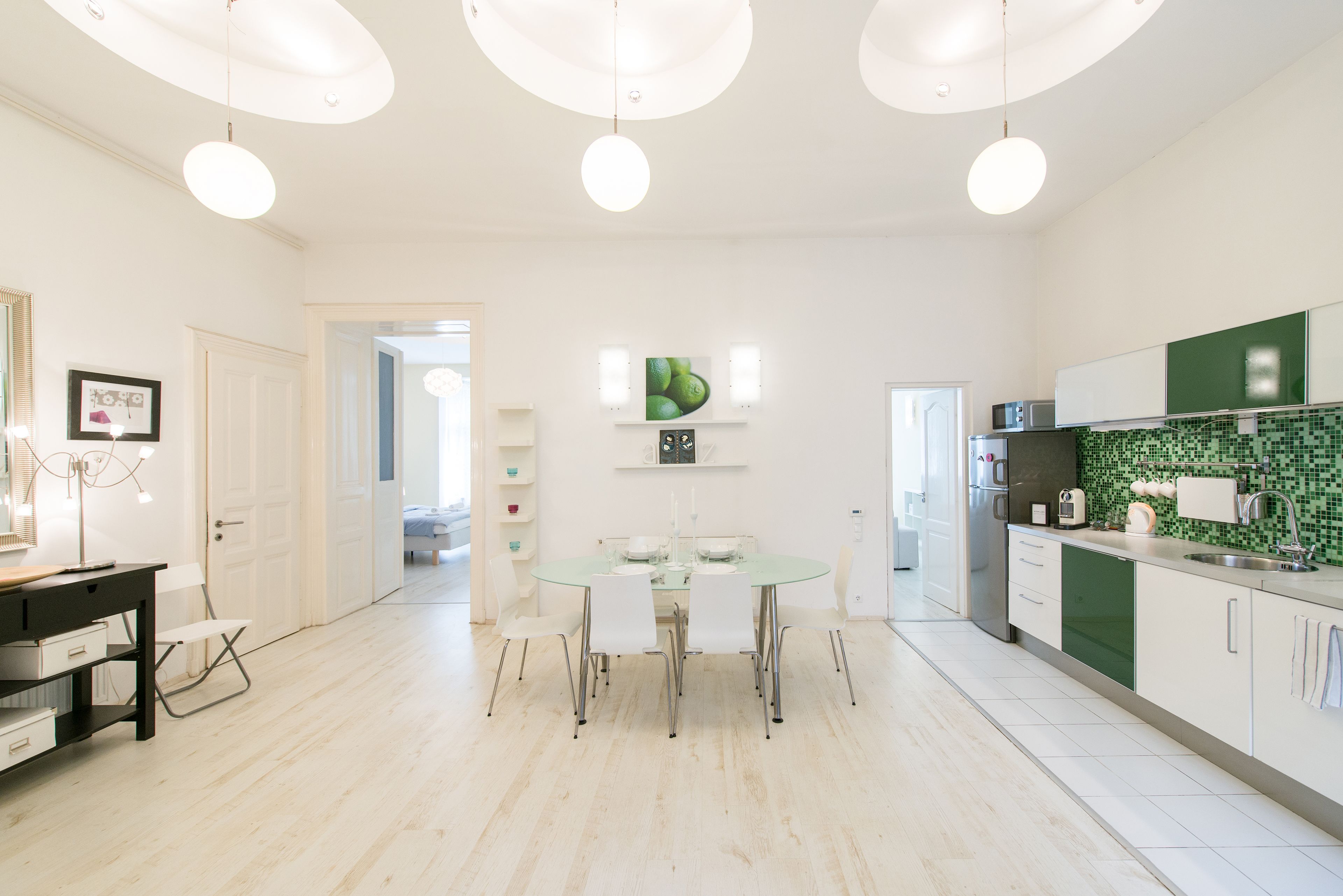 Une cuisine moderne avec des meubles blancs, un pare-feu vert et une table à manger en verre, accompagnée de chaises.