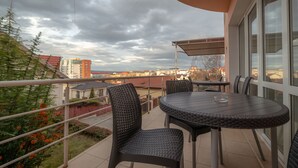 Un balcón con una mesa redonda y sillas, con vistas a un paisaje urbano que incluye edificios y un cielo nublado.