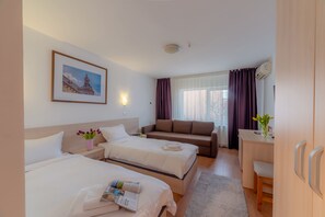 Habitación de hotel con dos camas, un sofá, un escritorio y una ventana con cortinas.