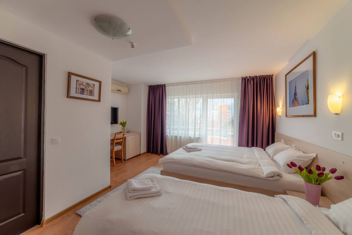 A hotel room with two beds, a desk, a chair, and a window with curtains.