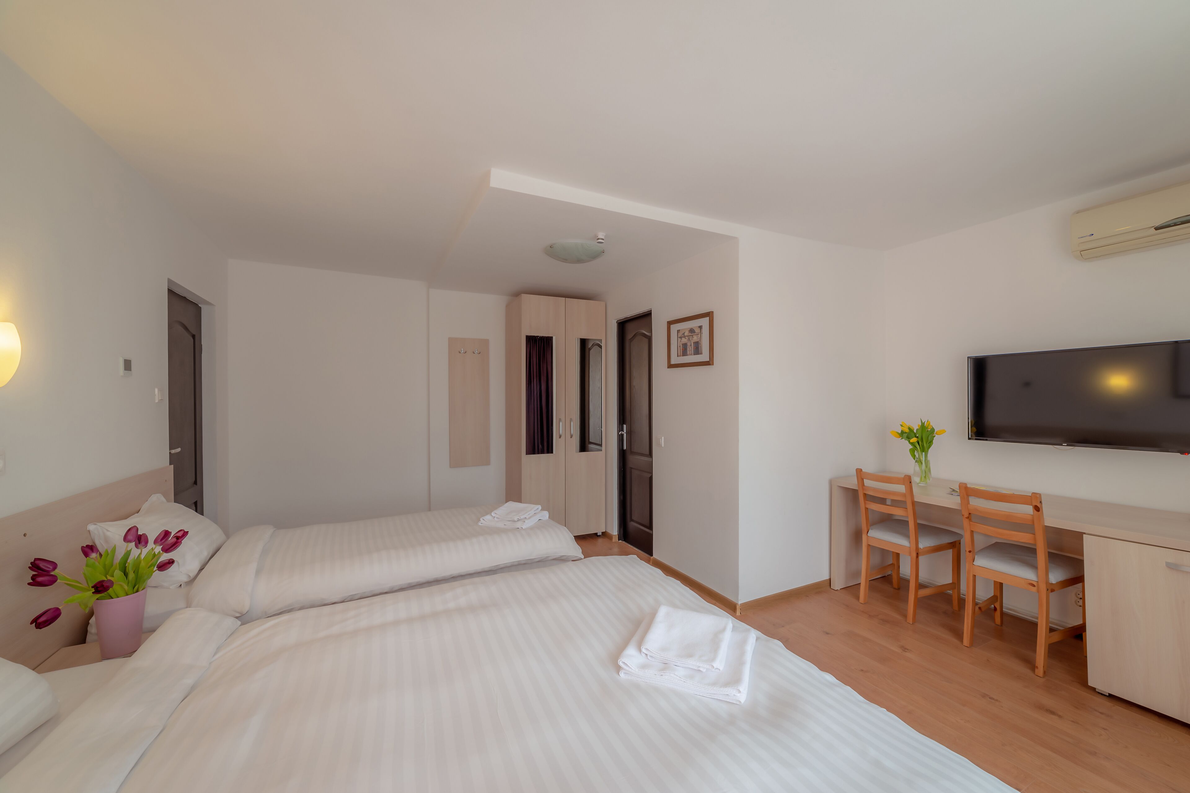 Una habitación de hotel con dos camas, un escritorio con sillas, un televisor y un aire acondicionado.