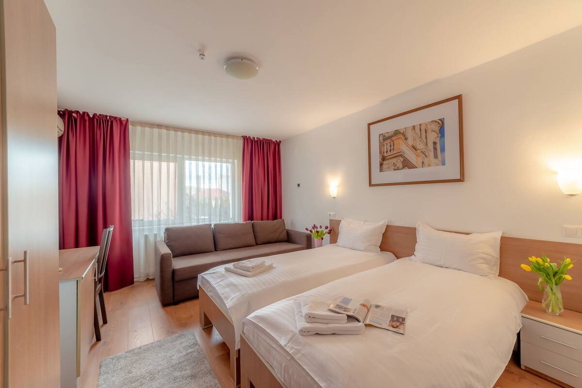 A hotel room with two beds, a sofa, a desk, and a window with curtains.