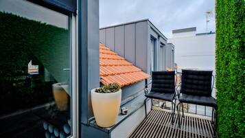 A modern outdoor balcony with a potted plant, two black chairs, and a red-tiled roof visible through the window.