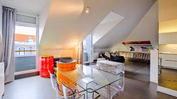 A modern apartment with a glass dining table, a sofa, and a kitchen area.