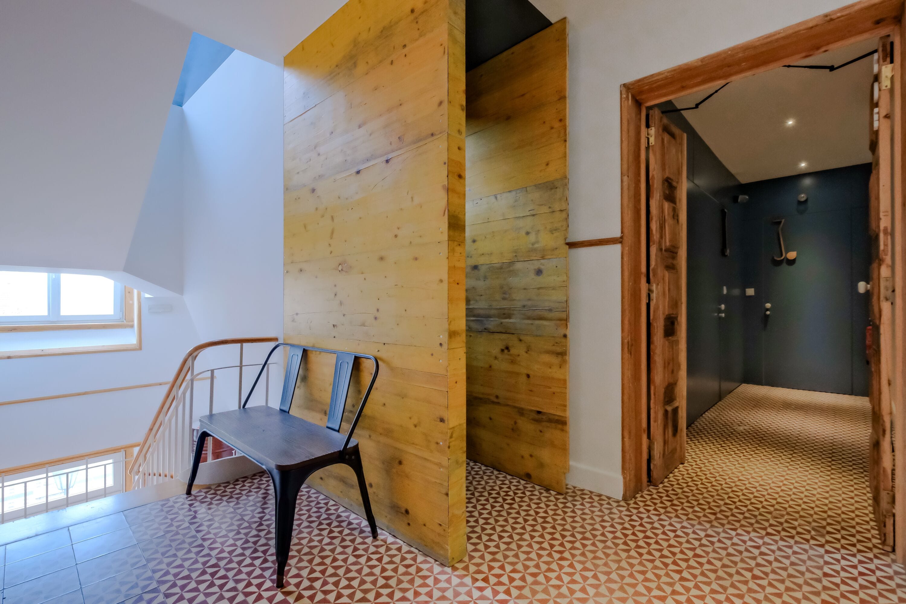 A modern interior with a wooden bench, geometric patterned floor, and a staircase leading to a dark room with a door.