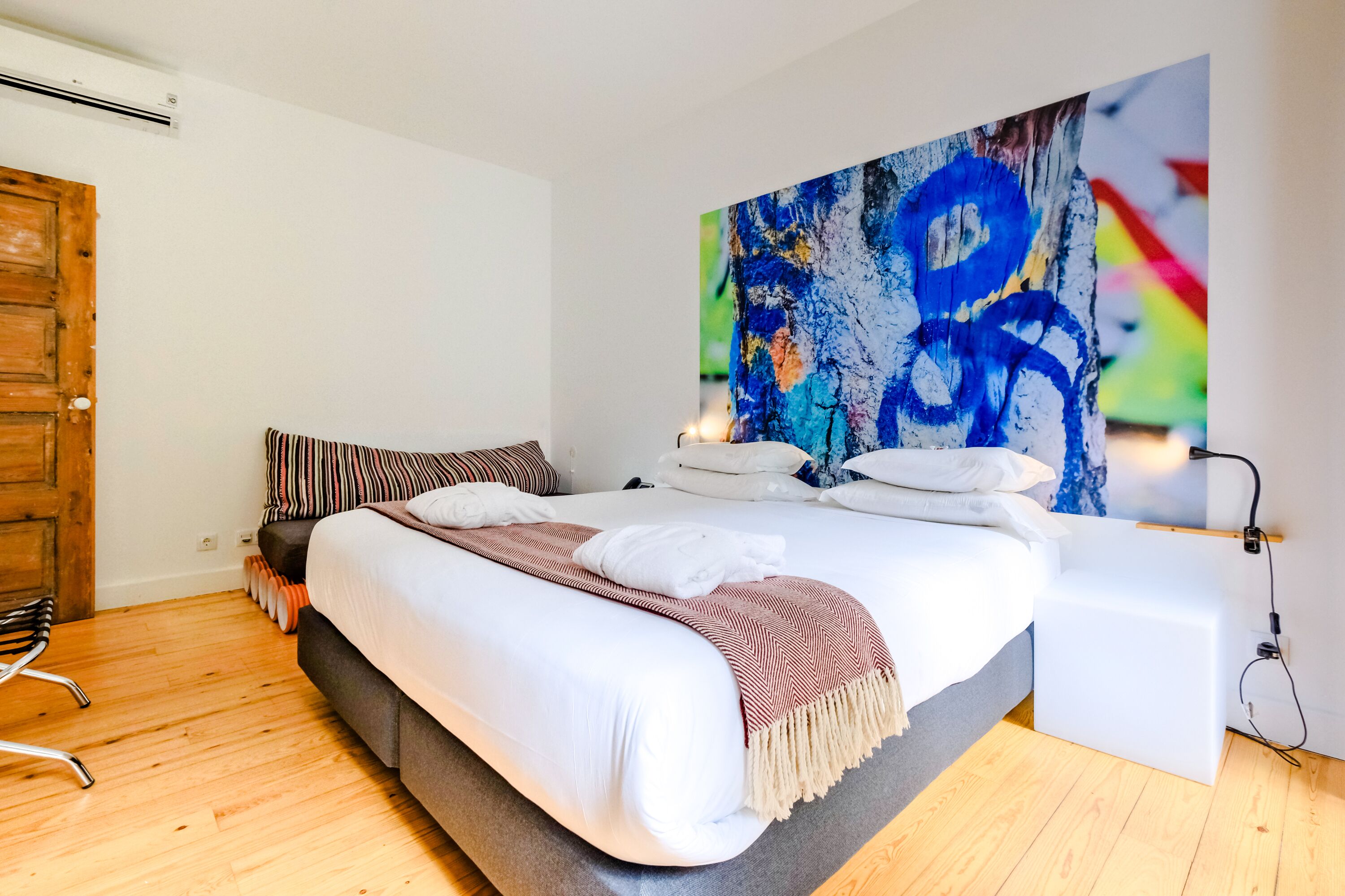 Ein modernes Schlafzimmer mit einem großen Bett, einer Holztür und einem farbenfrohen, abstrakten Gemälde an der Wand.