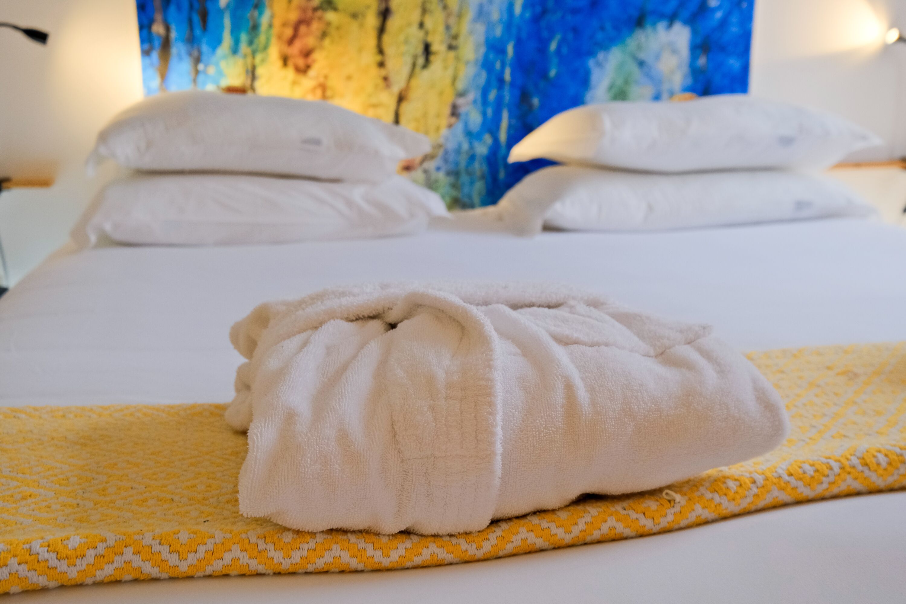 Un lit bien fait, avec des draps blancs et une serviette pliée posée sur une couverture à motifs jaunes.