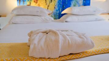 Un lit bien fait, avec des draps blancs et une serviette pliée posée sur une couverture à motifs jaunes.