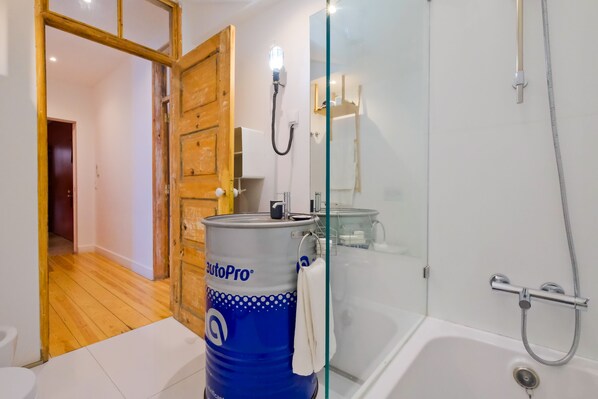 Baño con bañera, ducha y retrete. Se observa un barril azul grande con el logotipo de AutoPro.