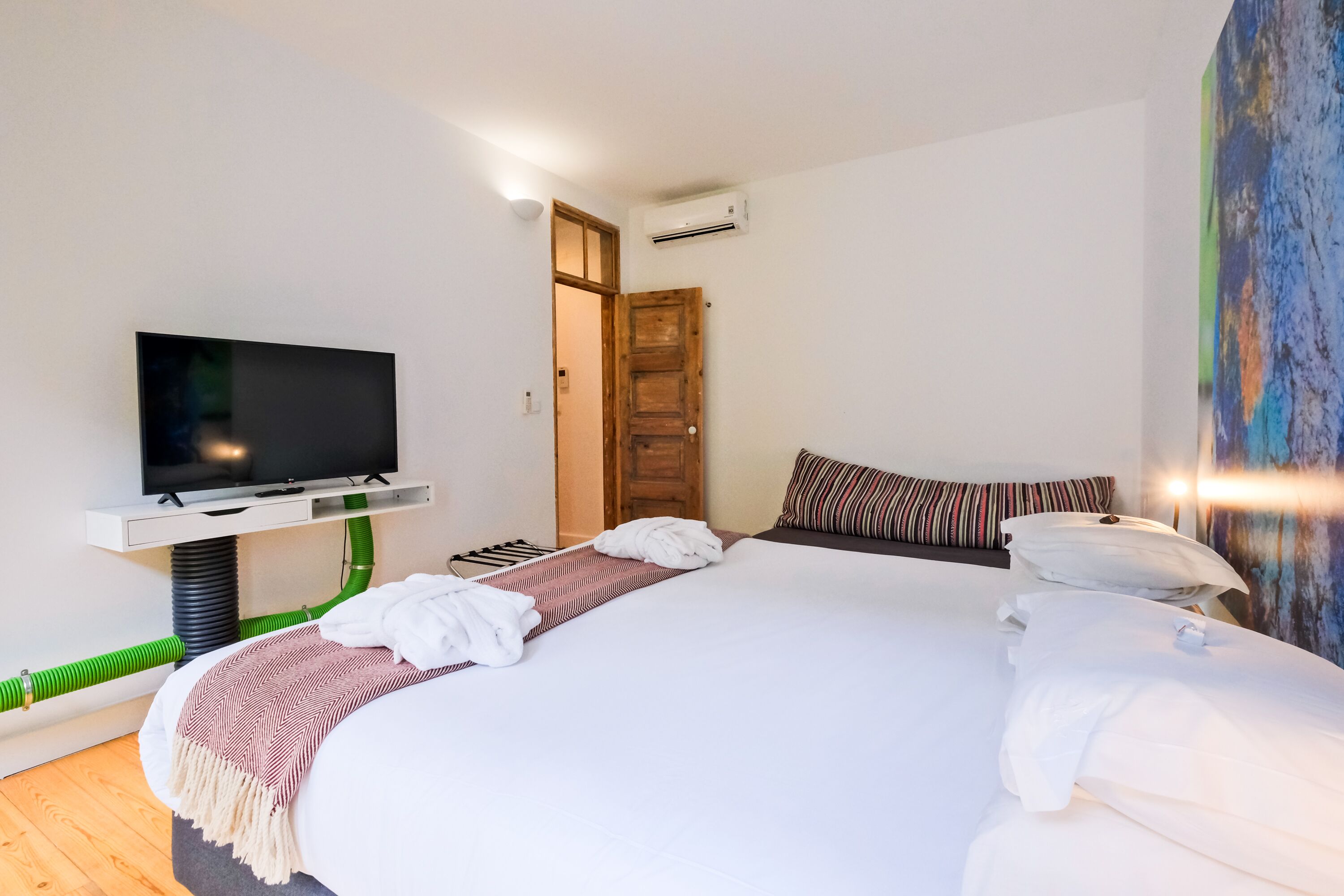 Ein modernes Hotelzimmer mit einem großen Bett, einem Flachbildfernseher, einer Holztür und einem Gemälde an der Wand.
