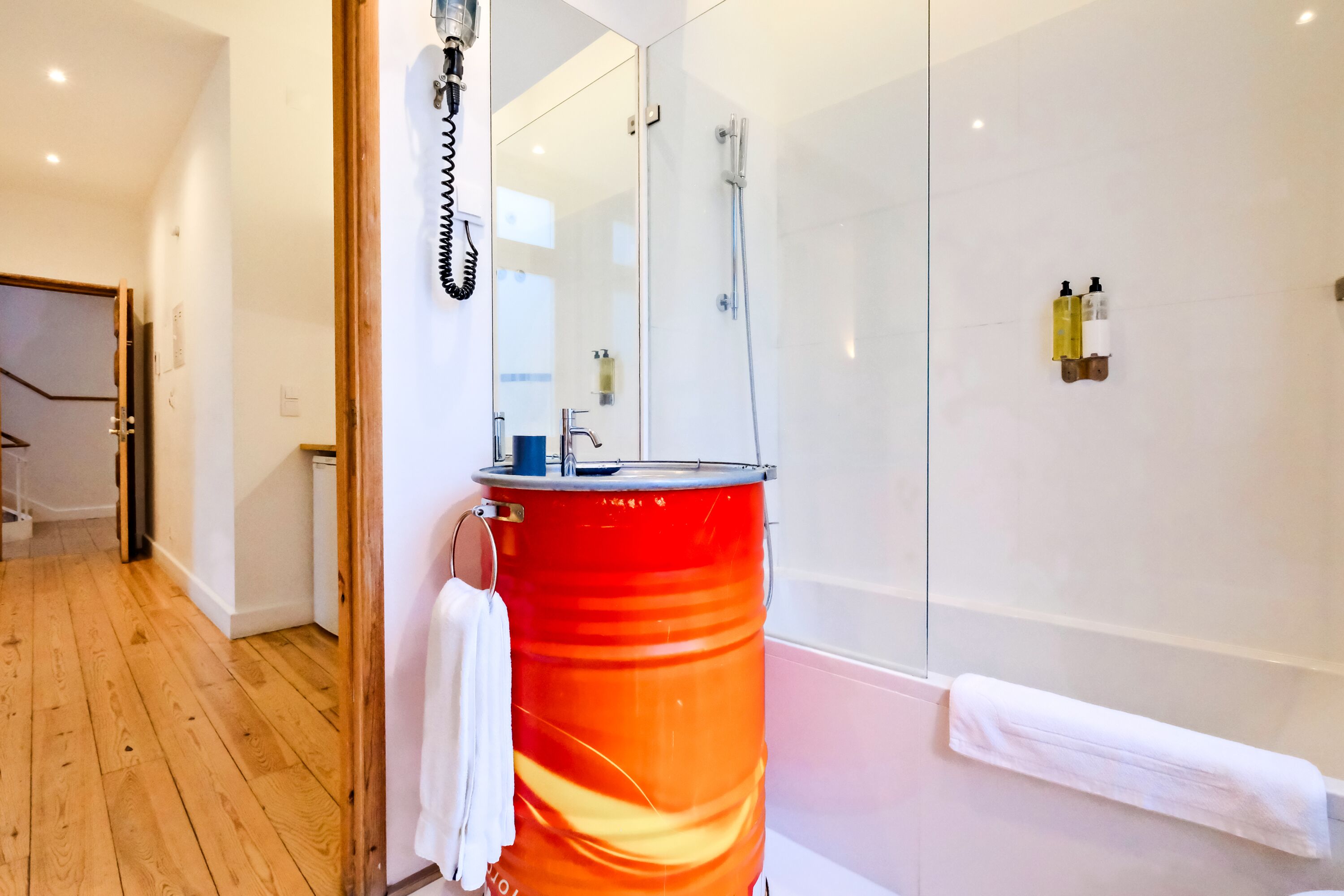 A modern bathroom with a glass shower enclosure, a red barrel, and a white towel hanging on the door.