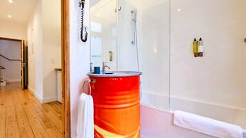 A modern bathroom with a glass shower enclosure, a red barrel, and a white towel hanging on the door.