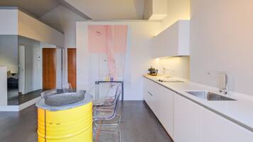 Una cocina moderna con armarios blancos, un lavamanos de acero inoxidable y un barril amarillo.