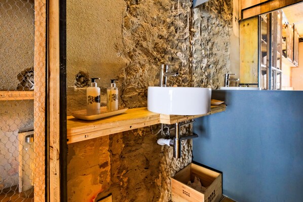 Un baño rústico con pared de piedra, encimera de madera y lavamanos blanco.